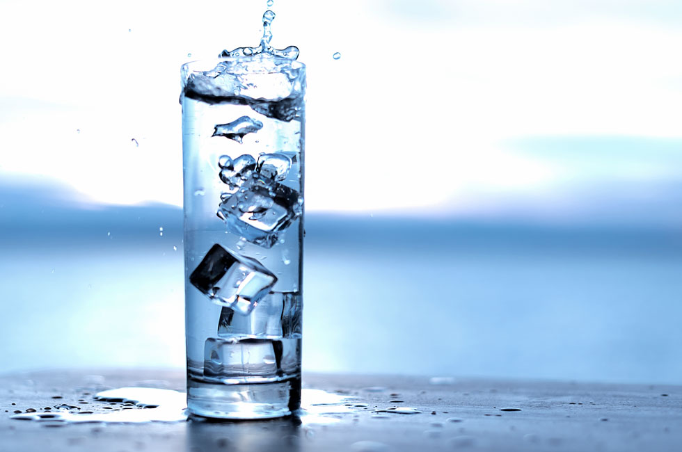 A glass of water with ice cubes reflecting light, symbolizing the power of water in rituals for success and wealth.